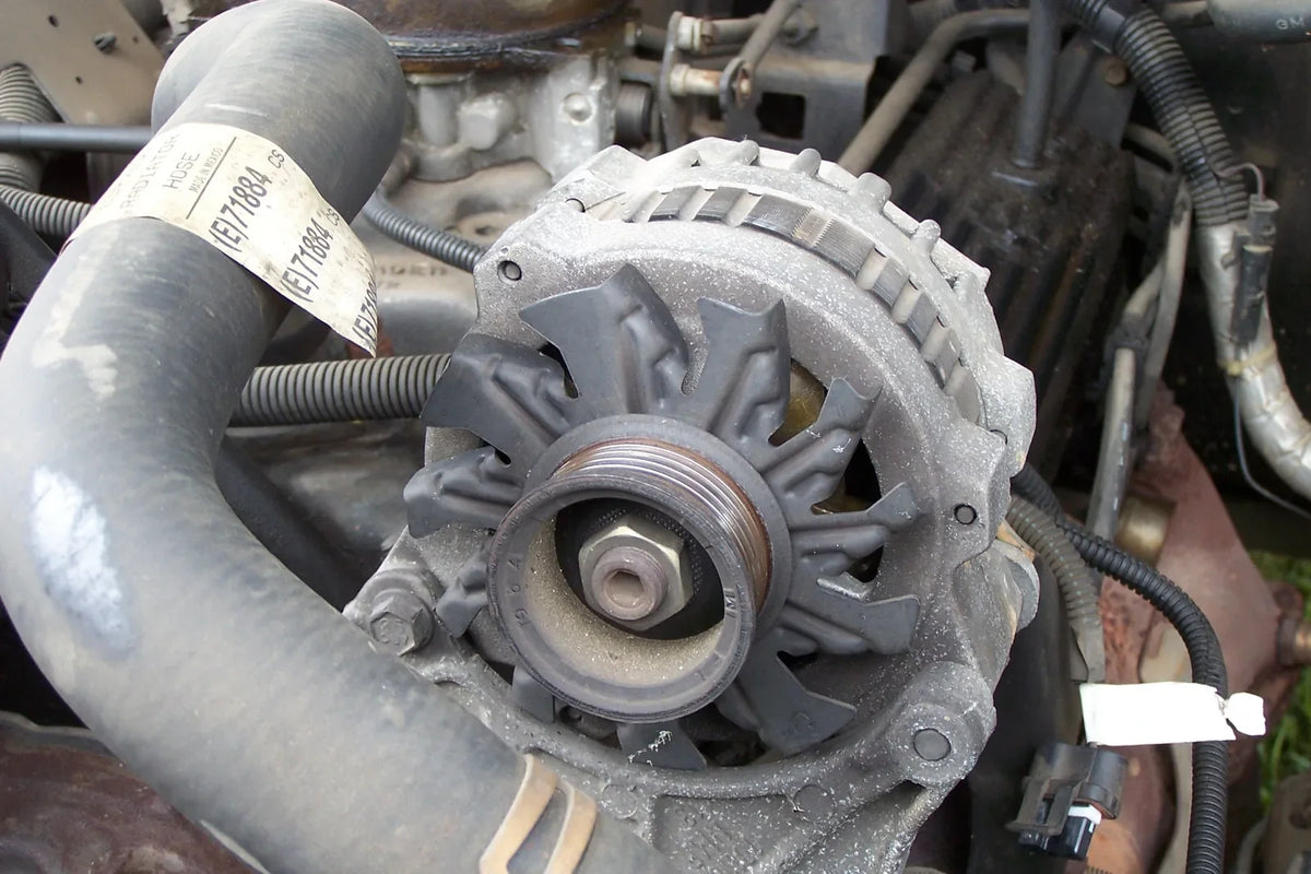 Close-up of an automotive alternator with its pulley exposed and drive belt removed.